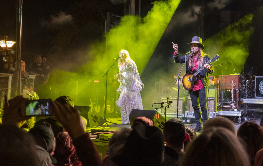 A photography of Lukas Nelson and Margo Price performing on stage in front of a crowd watching and taking photos.